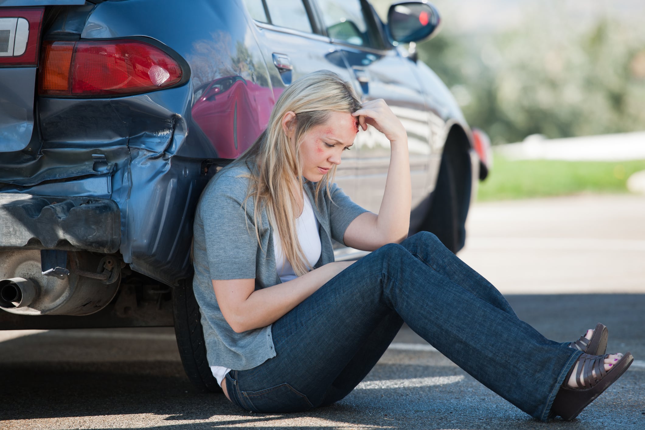 A woman leaning against her car after a car accident.
