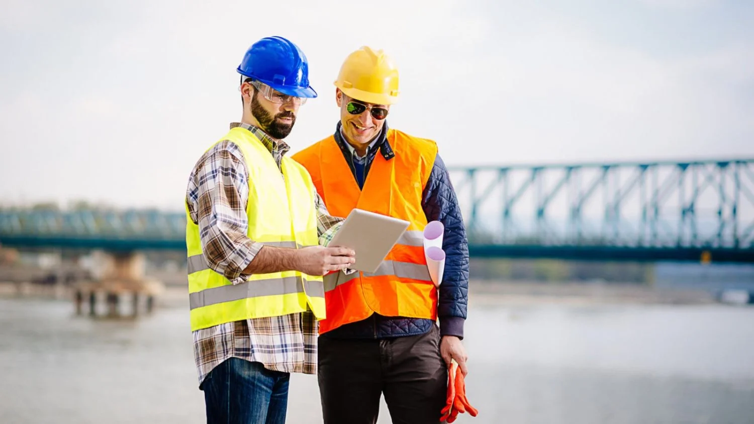 Two construction workers read from a tablet on the job site.