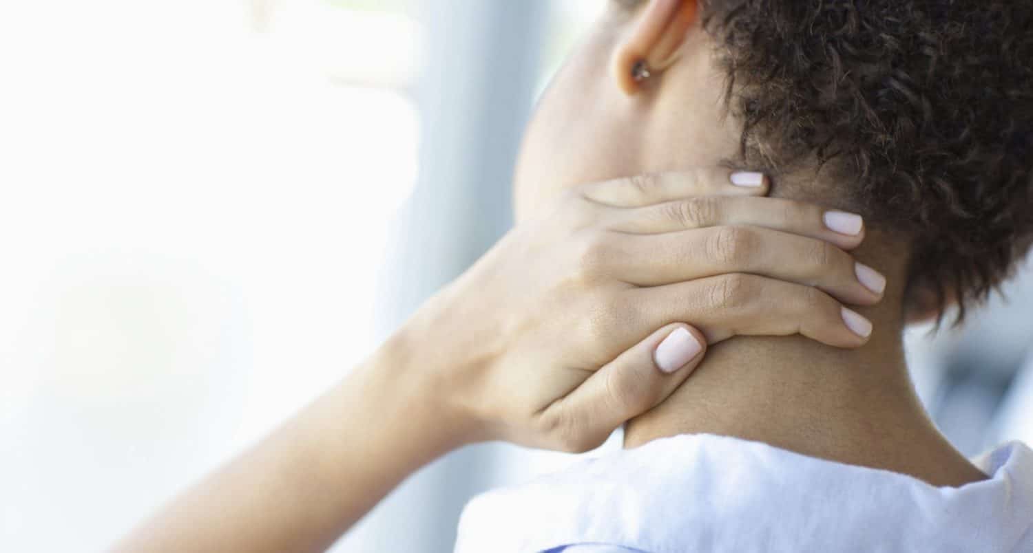 An individual with curly hair holding the back of their neck as if in pain.