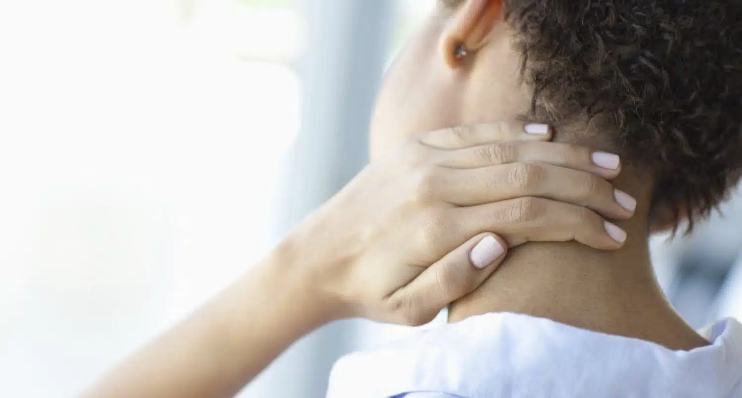 An individual with curly hair holding the back of their neck as if in pain.