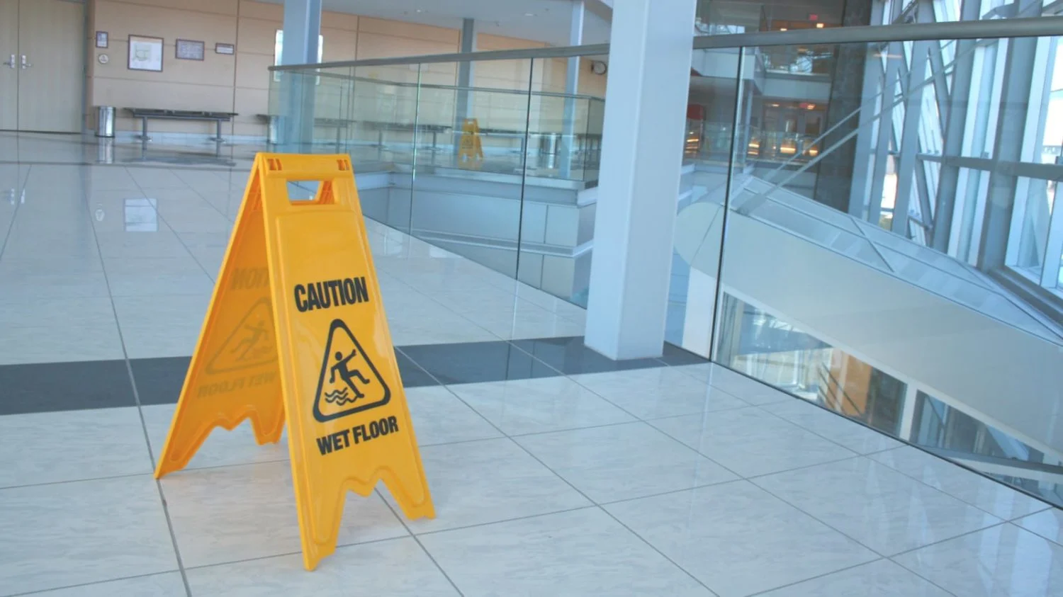 A yellow “CAUTION: WET FLOOR” sign stands on the floor of a building.