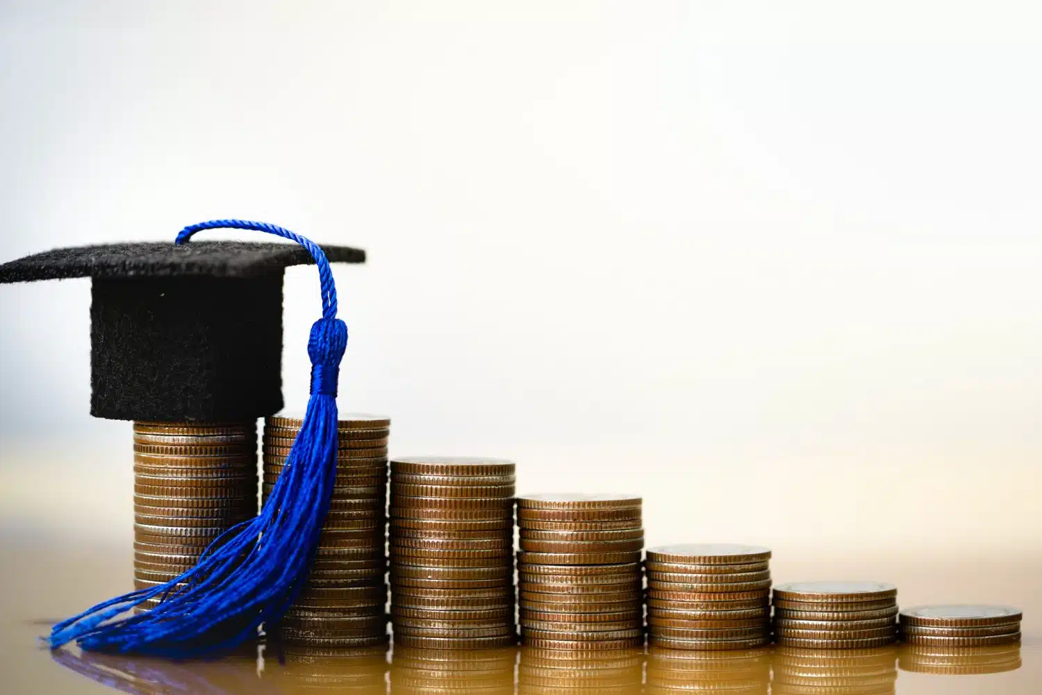 A graduation cap propped on stacks of coins.