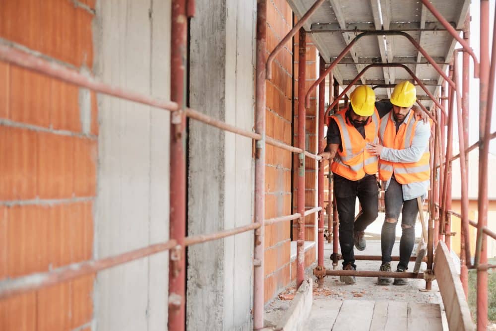 A construction worker helping his coworker walk after an injury.