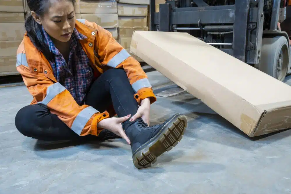 A woman working in a warehouse holding her ankle in pain.