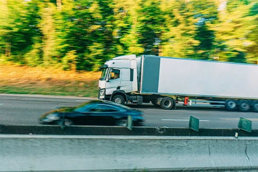 A black sedan passes a big truck on the left side, leaving one lane free between them.