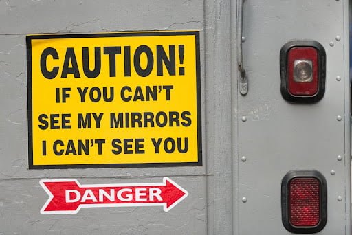 A sign on a tractor-trailer with large blind spots says “CAUTION! If you can’t see my mirrors, I can’t see you”.