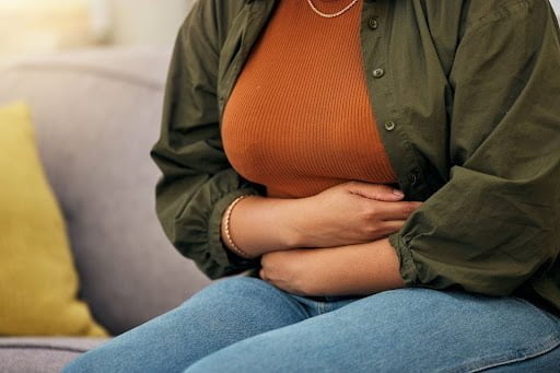 A woman is holding her stomach due to abdominal pain.