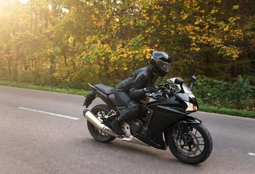 A biker in all black on a black motorcycle, driving down the road.