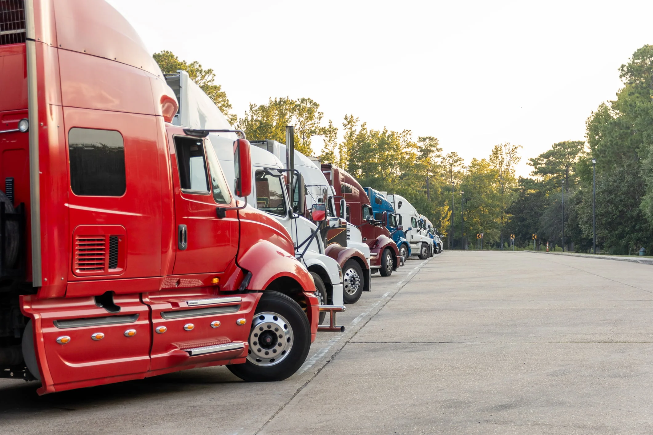 A line of semi-truck cabs are seen in a large parking lot.