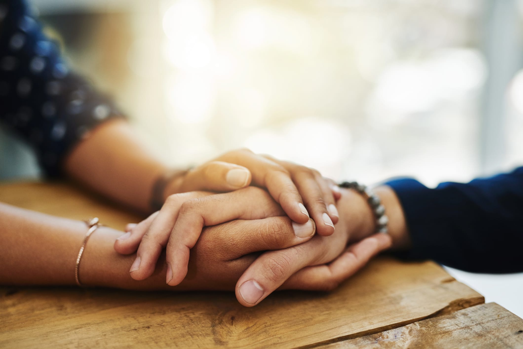 Two people hold hands, indicating one person comforting the other in their time of grief.