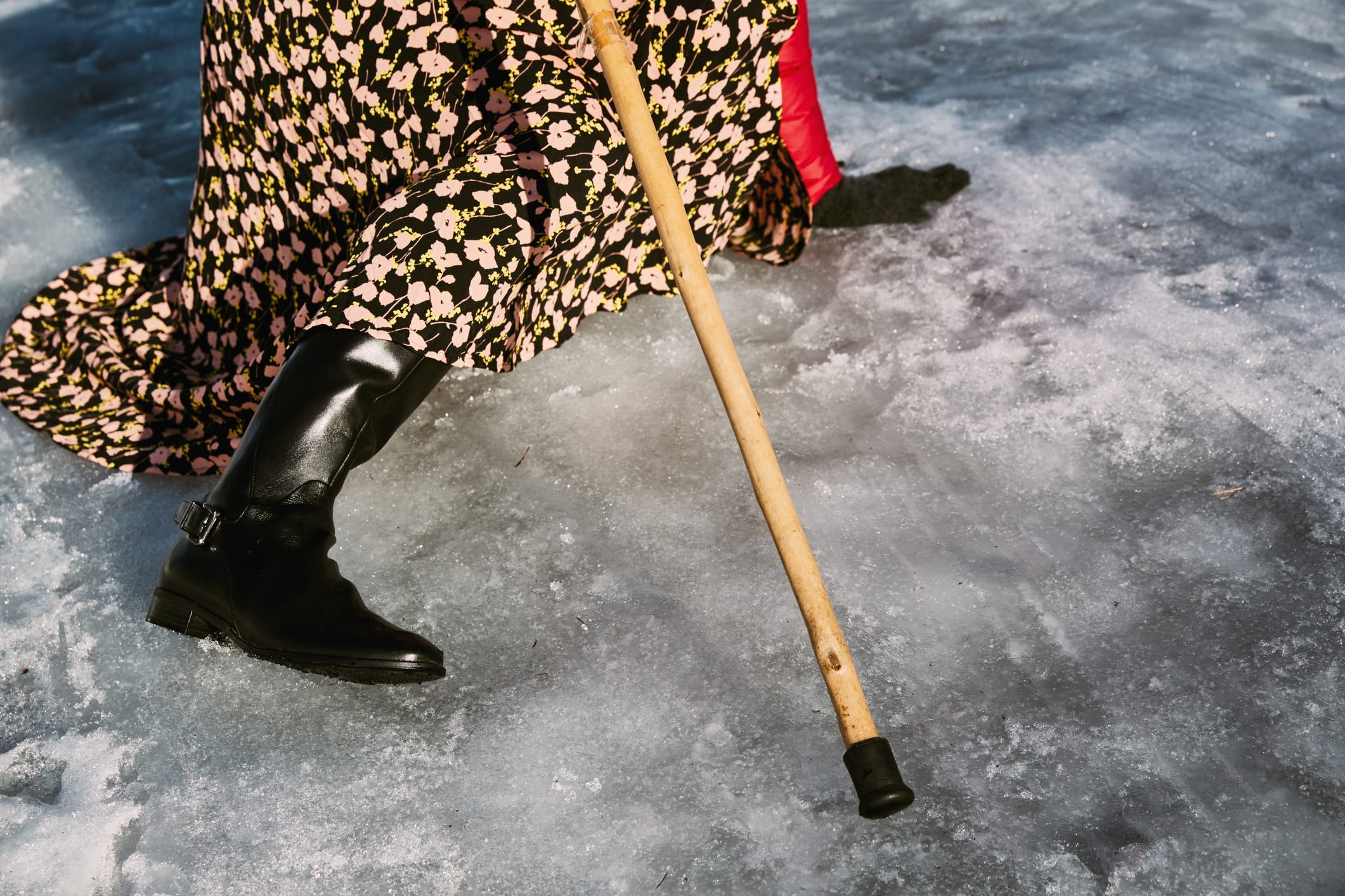 An individual with a walking stick has fallen on an icy road.