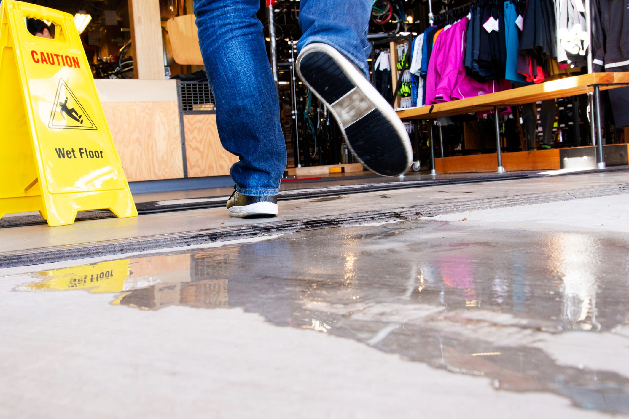 An individual appears to be falling on a puddle next to a wet floor sign.
