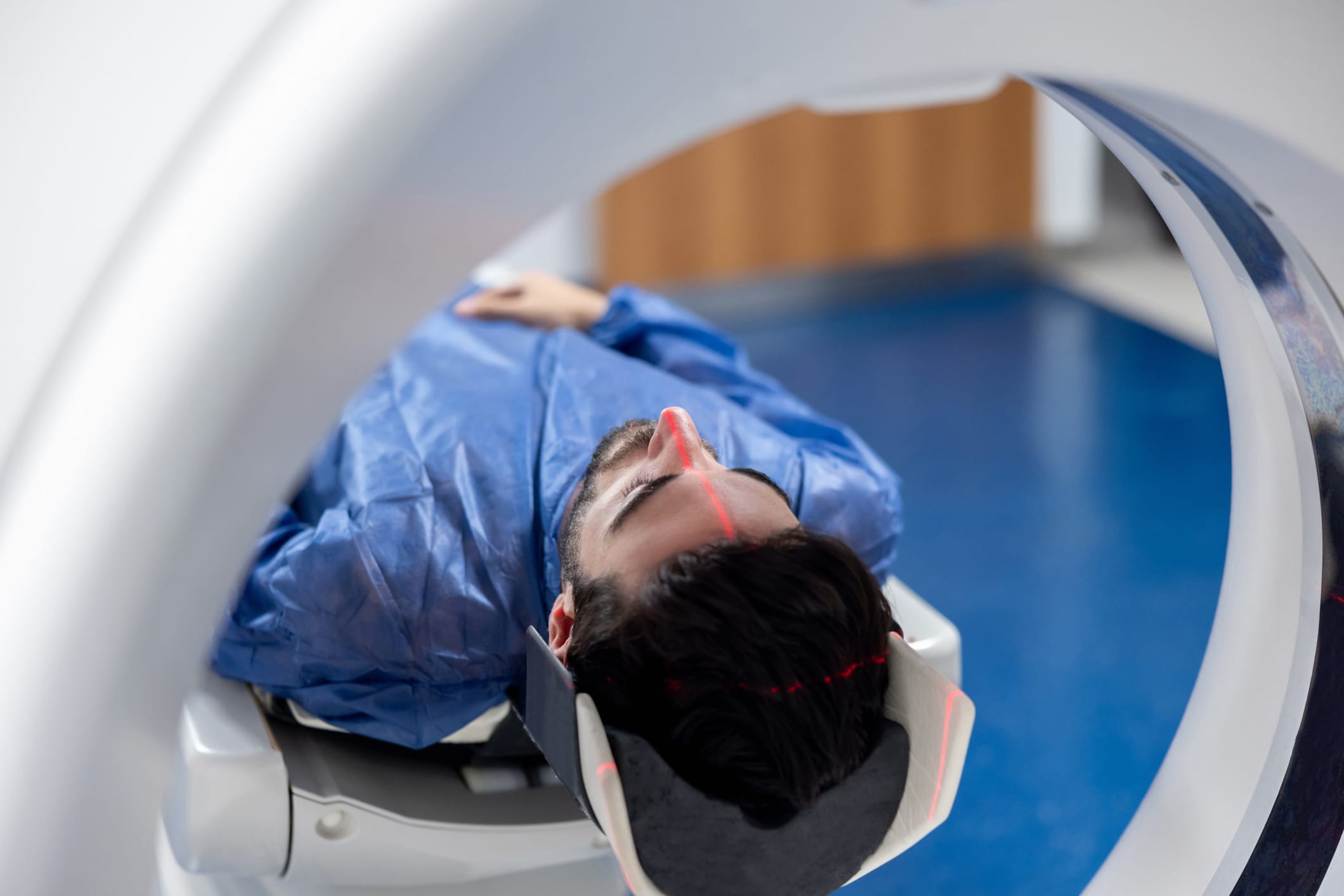 A man in a blue hospital gown is entering an MRI machine for a brain scan.