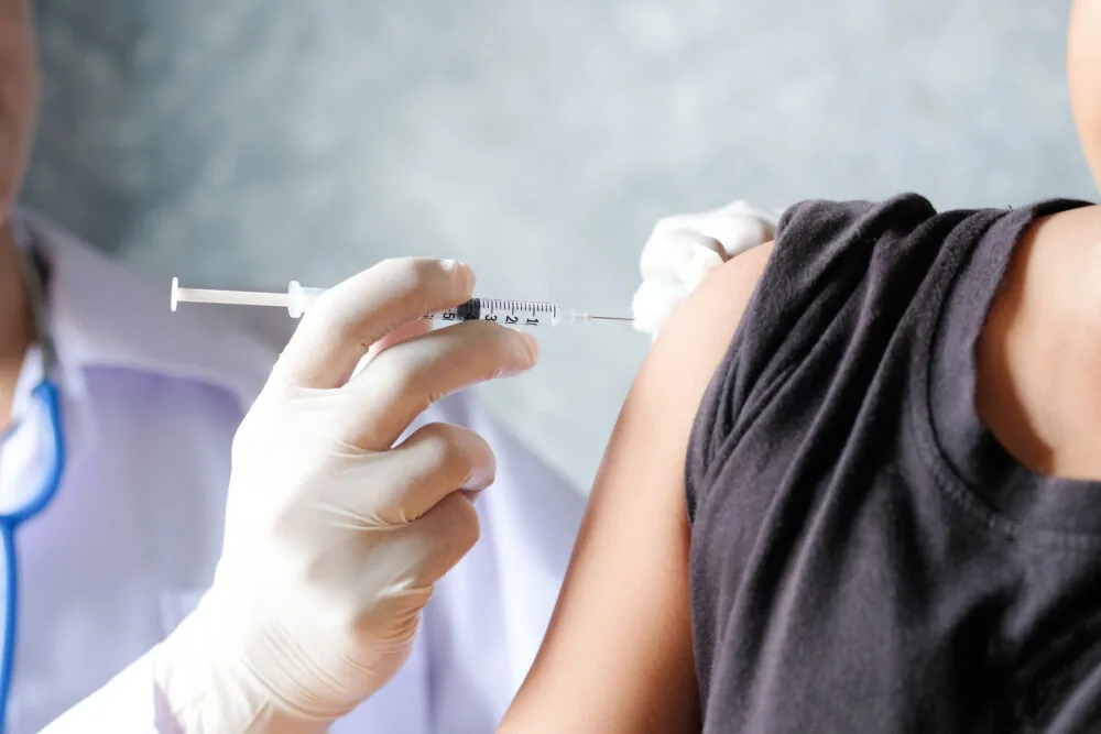 The gloved hand of a physician administering a Depo-Provera® shot into the upper arm of a patient.