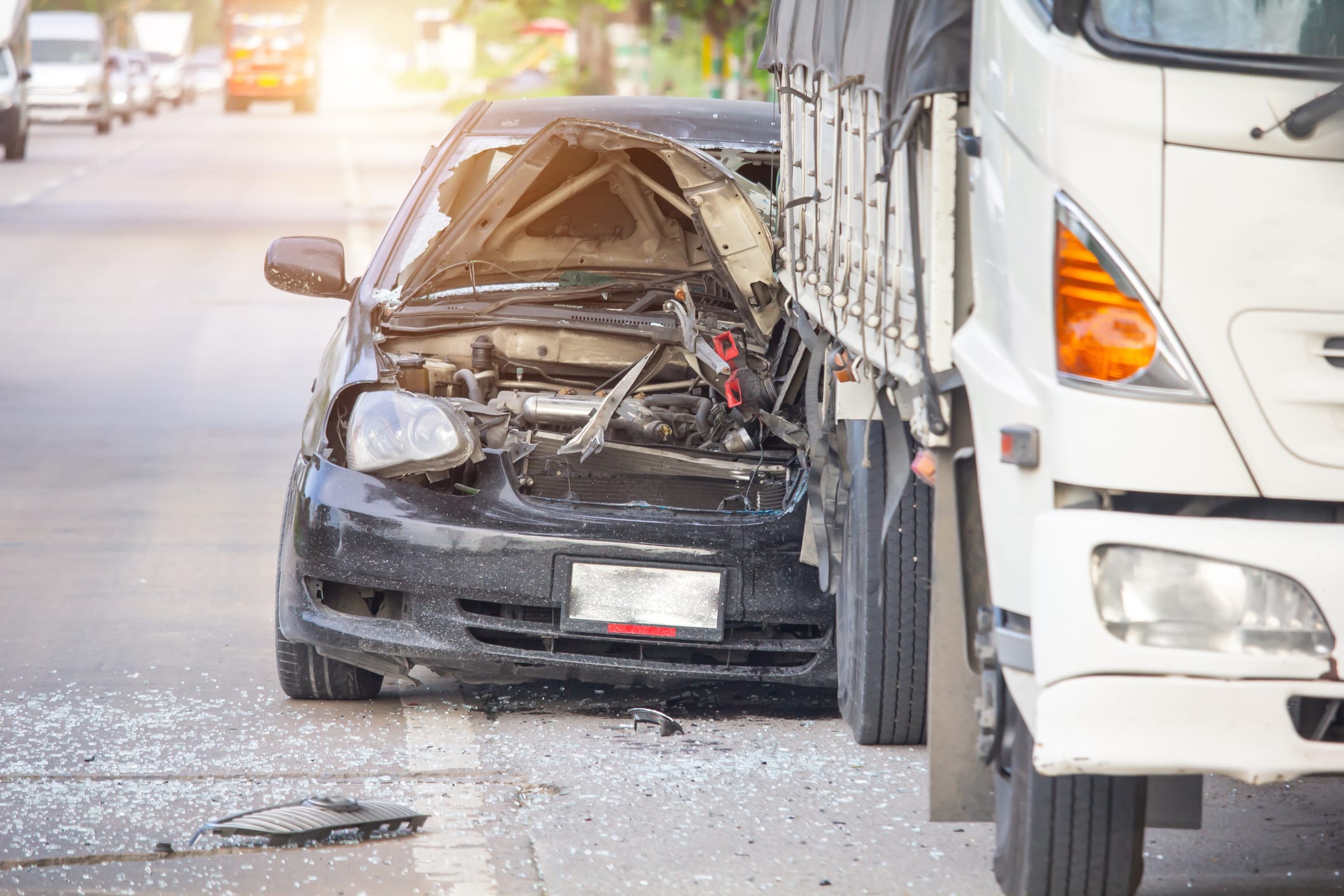 A black car with severe front-end damage is shown after a crash with a white truck on a road, with debris scattered around.