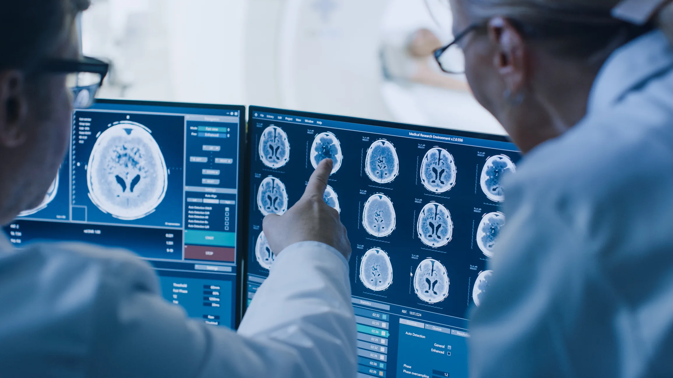 Two doctors reviewing brain scans and MRI results on computer monitors.