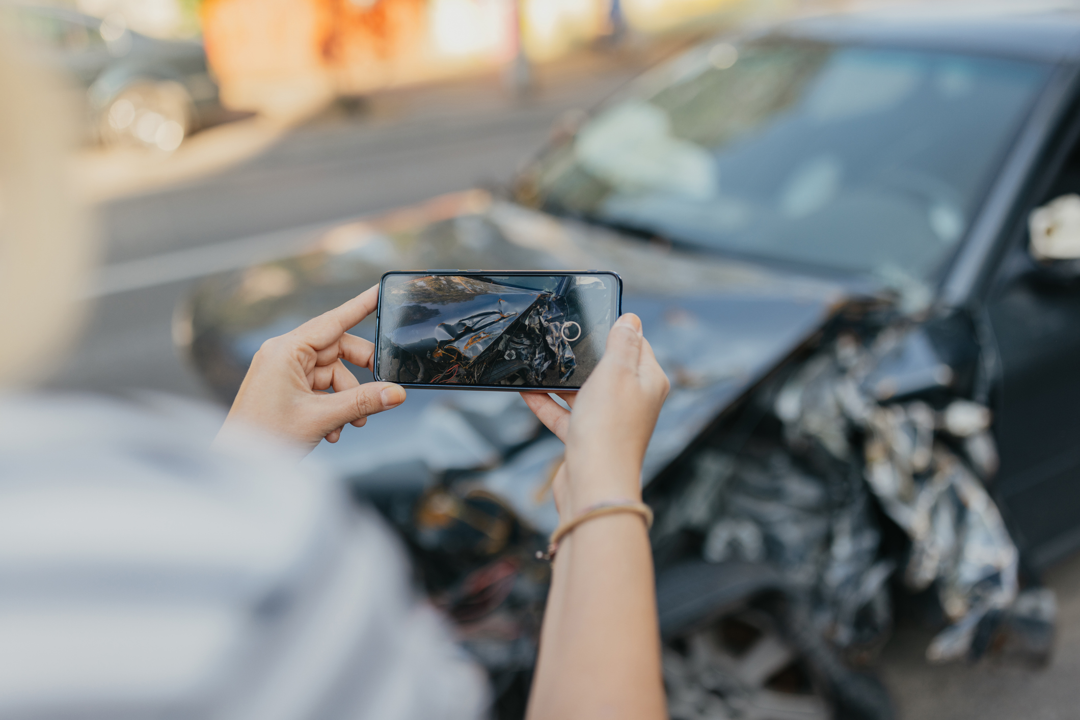Person using their phone to take a picture of a wrecked car as evidence after a car accident.