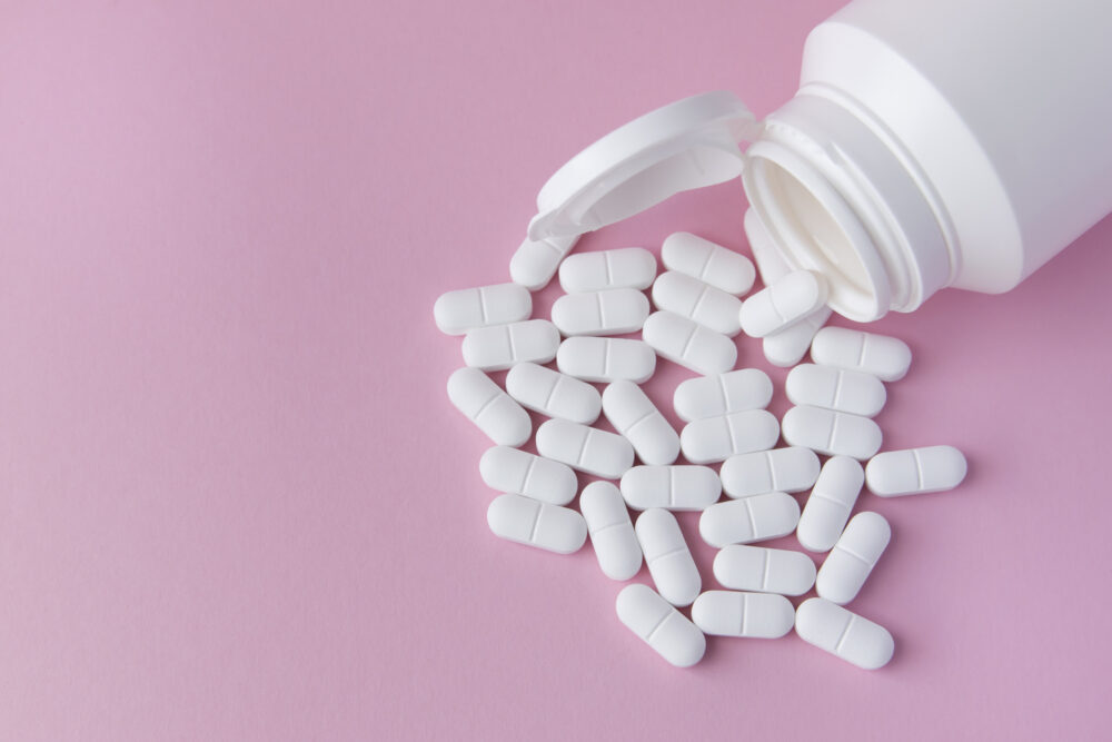 A white bottle with white acetaminophen tablets spilled over a pink background.