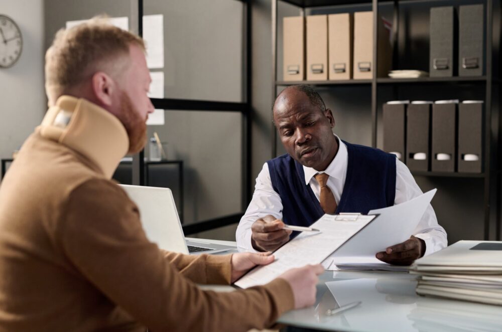 African-American attorney explains personal injury paperwork to client in a neck brace.
