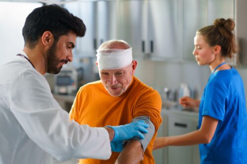 Older man with a head injury is treated by a doctor and nurse in Massachusetts after a car accident.