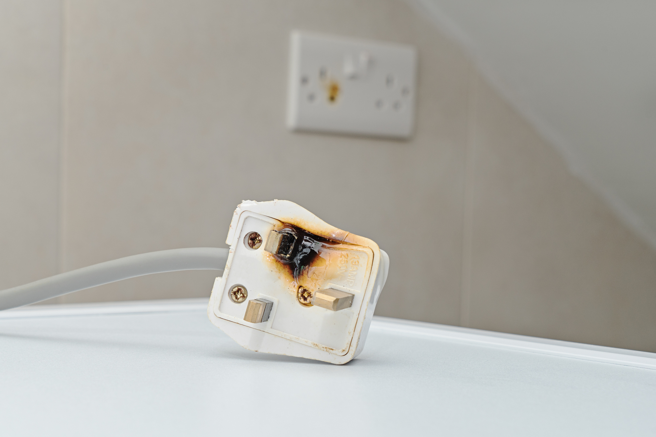 A burnt power plug with a burnt electrical socket in the background.