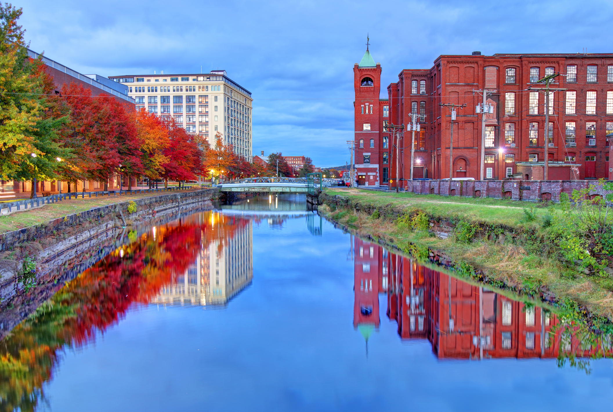 Trees and buildings reflect on a waterway in Lawrence, Massachusetts.