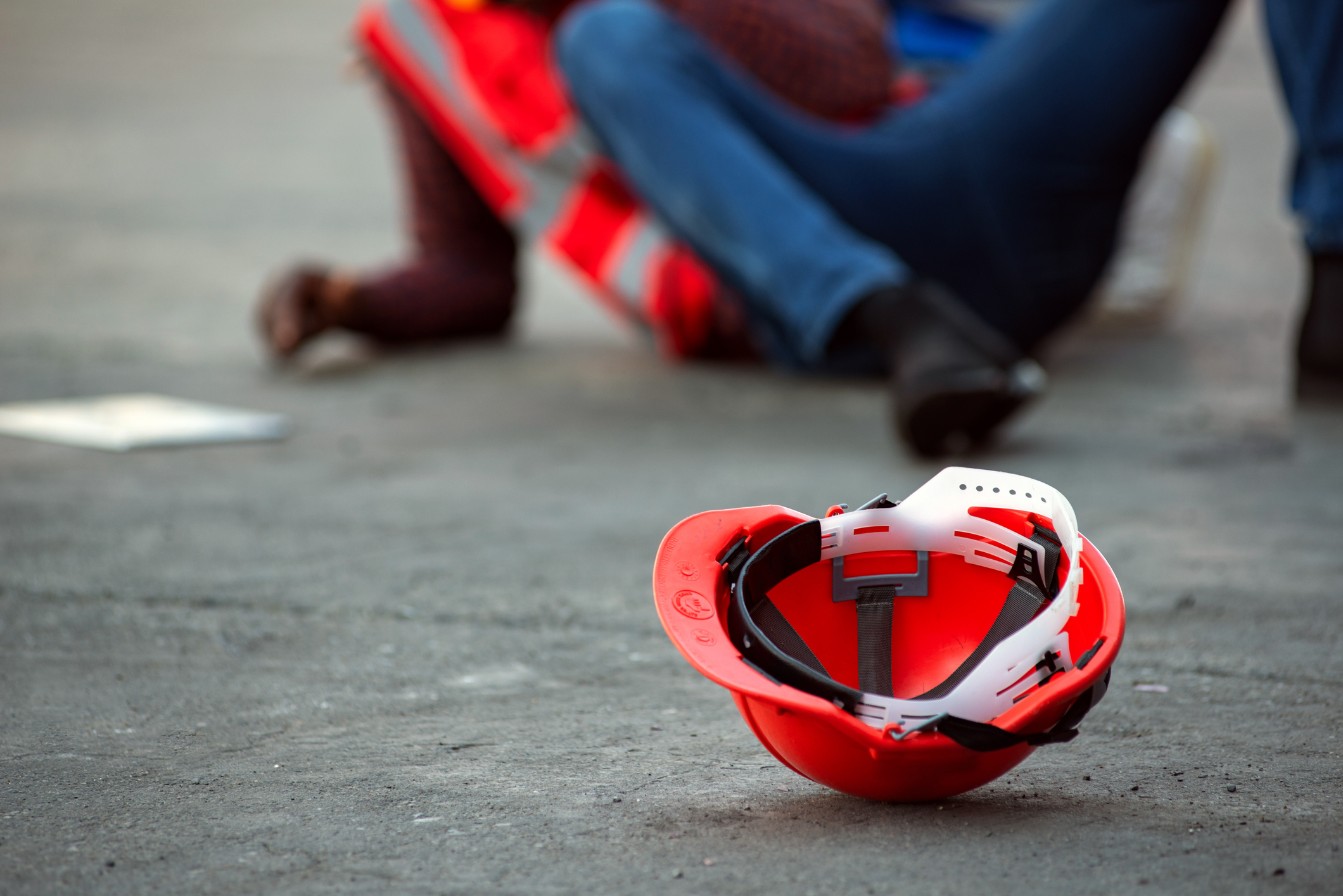 A hard hat with a fallen worker in the background.