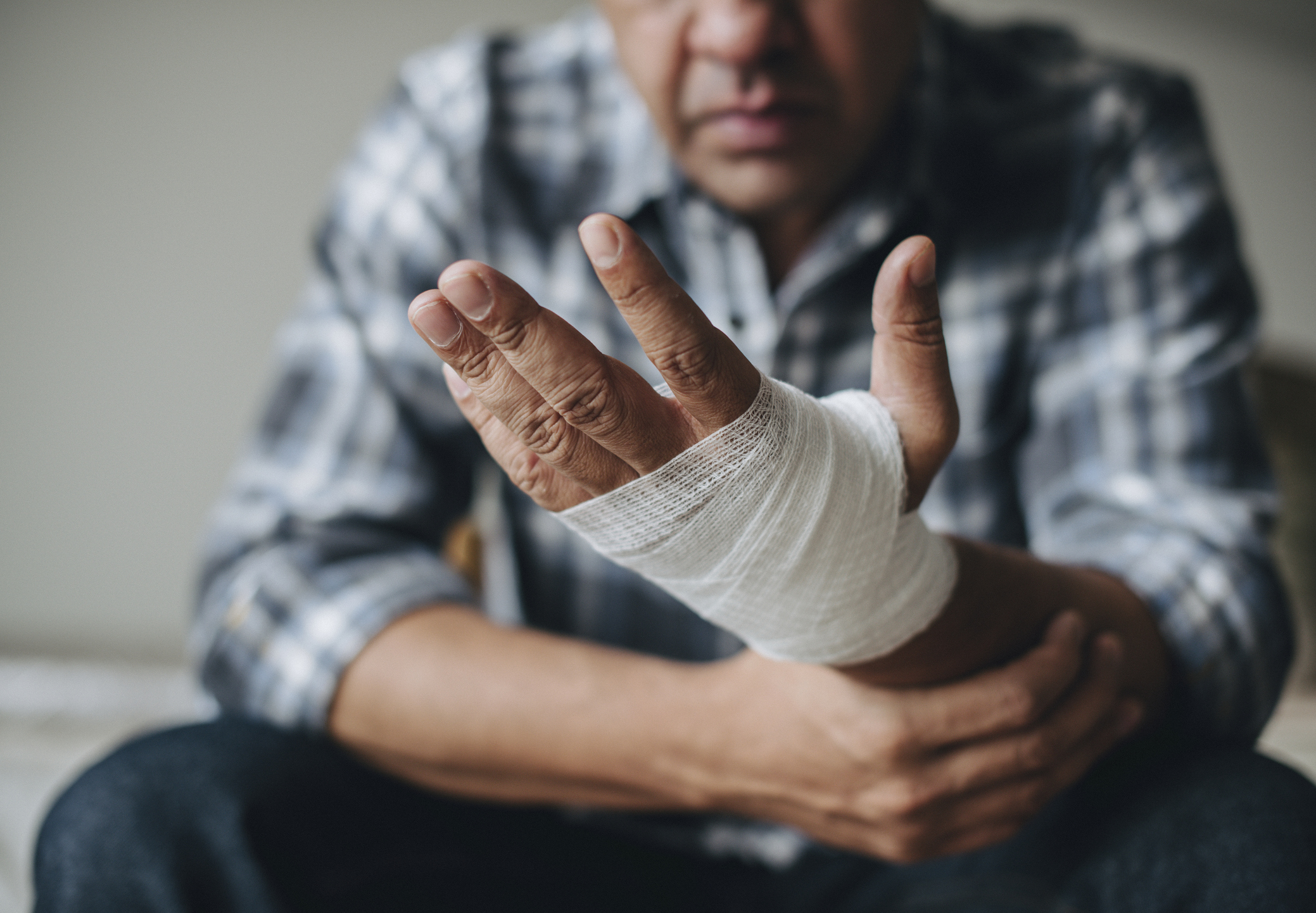 A man with a bandaged hand, holding his wrist with his unbandaged hand.