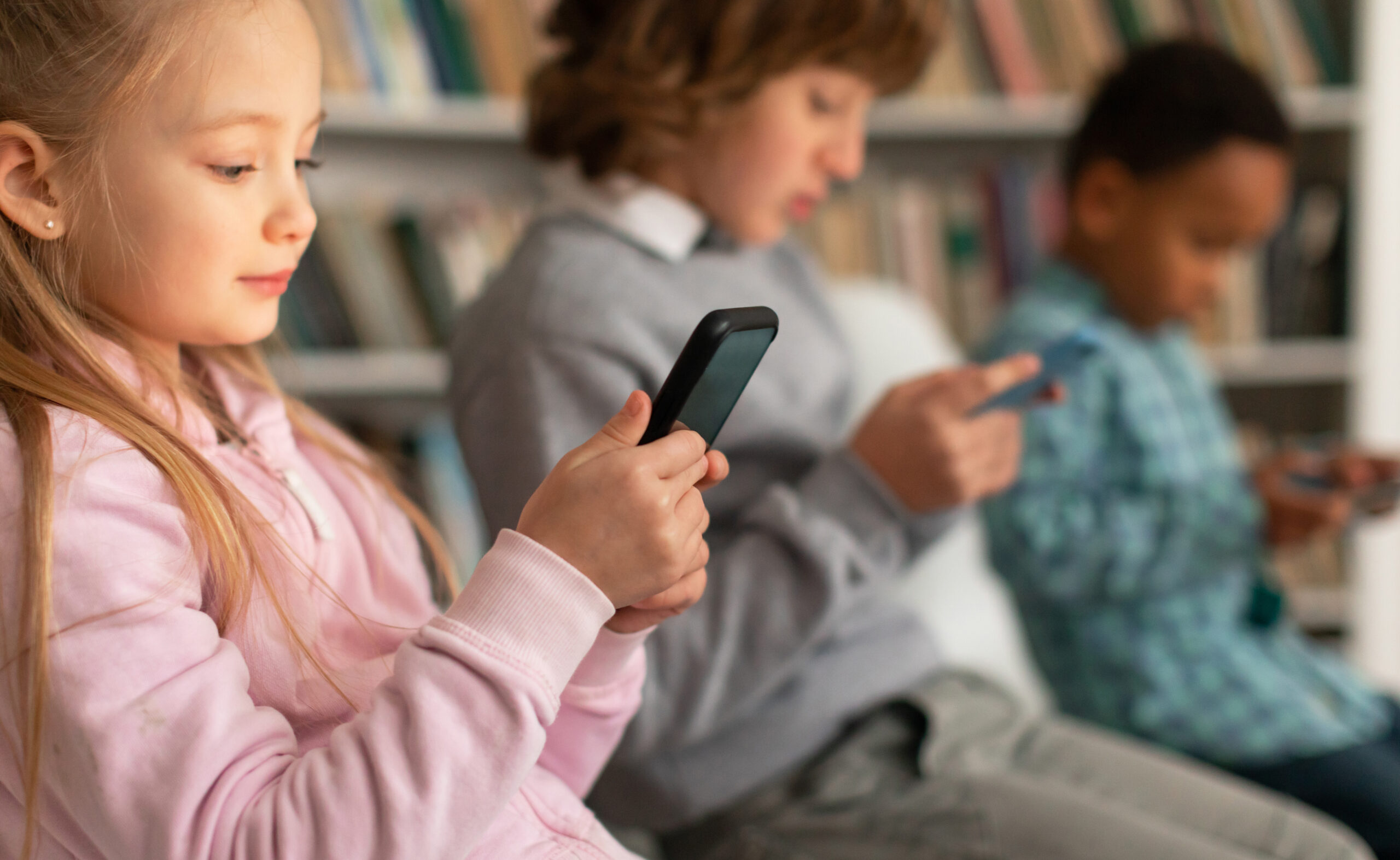 A group of children sitting in a library, all using their phones.