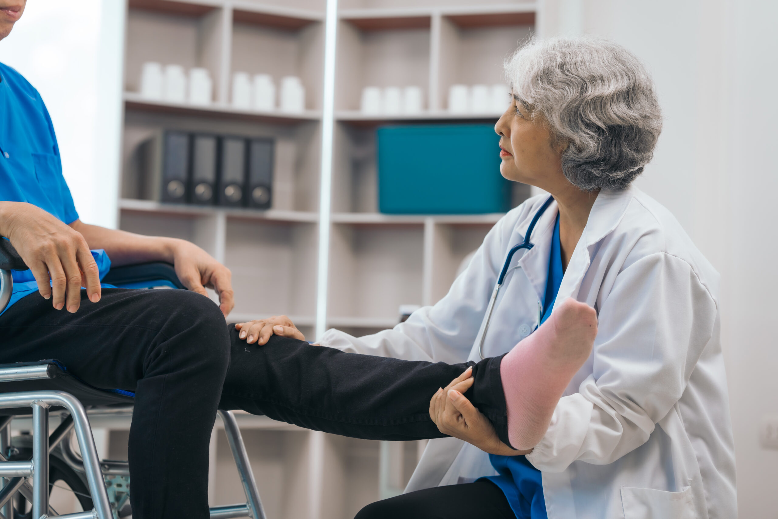 A medical professional tends to a patient in a wheelchair, holding their leg.