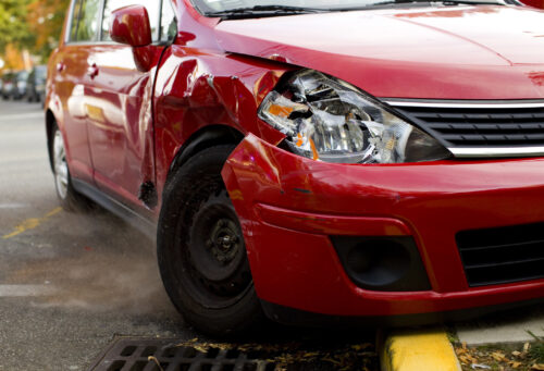 A red car with a damaged front end and a missing rim on the tire.
