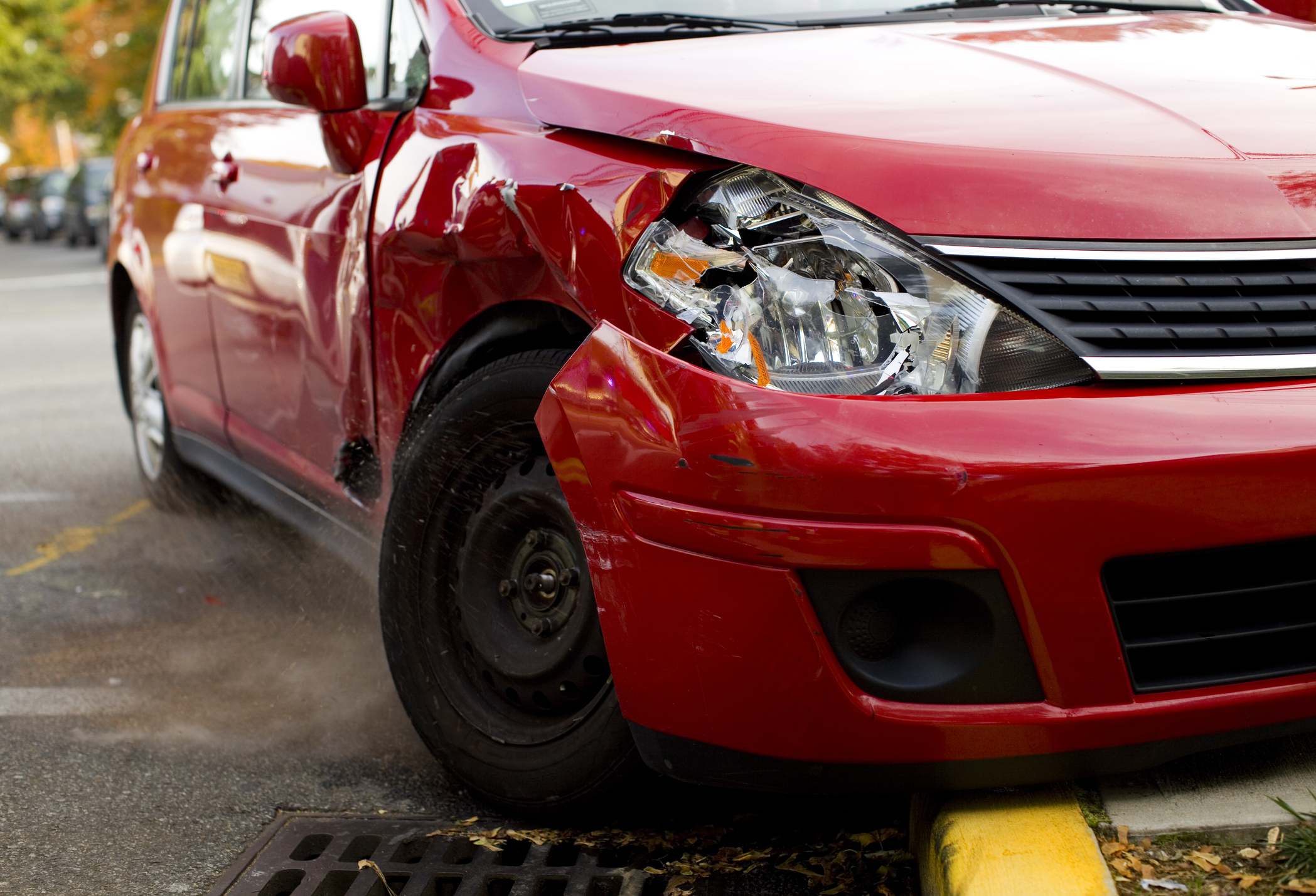 A red car with a damaged front end and a missing rim on the tire.