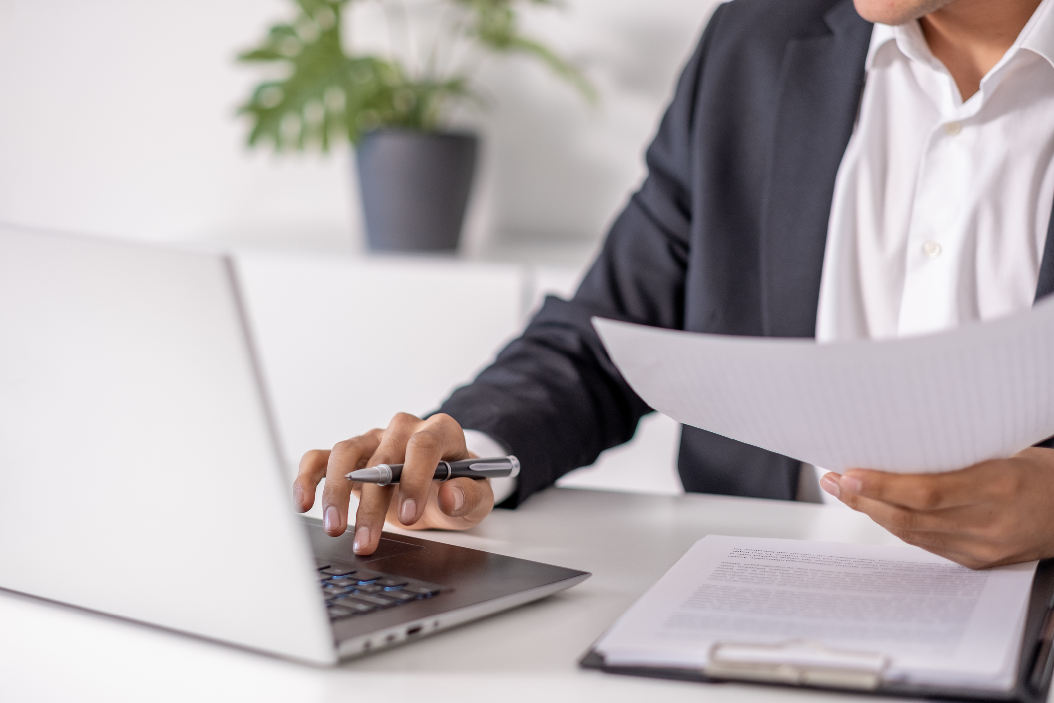 An attorney holding a document from his clipboard and typing on a laptop.