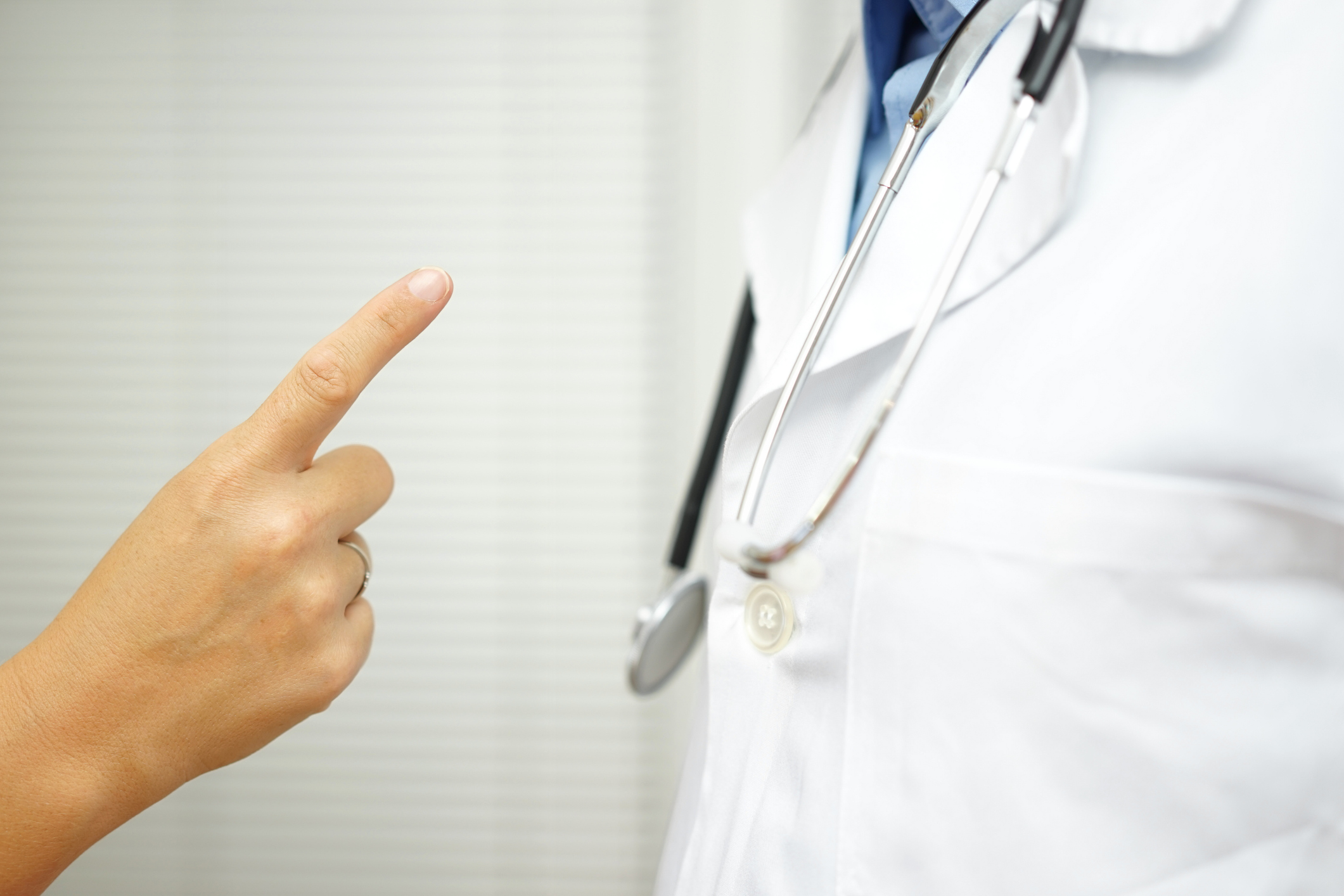 An individual points an accusing finger at a doctor who has a stethoscope around their neck.